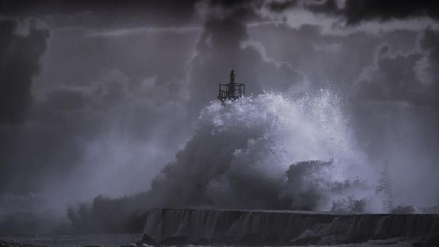 Big storm wave against lighthouse of Ave river mouth at sunset, Vila do Conde, north of Portugal. Enhanced sky. Toned blue.