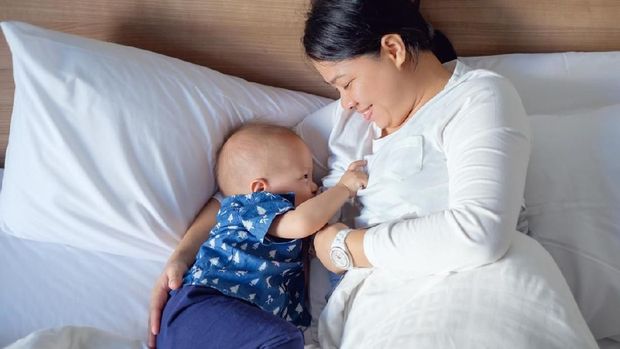 Mother breastfeeding baby son in bedroom and using mobile phone