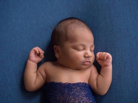 Sleeping, nine day old newborn baby boy swaddled in a blue wrap. Shot in the studio on denim blue material.
