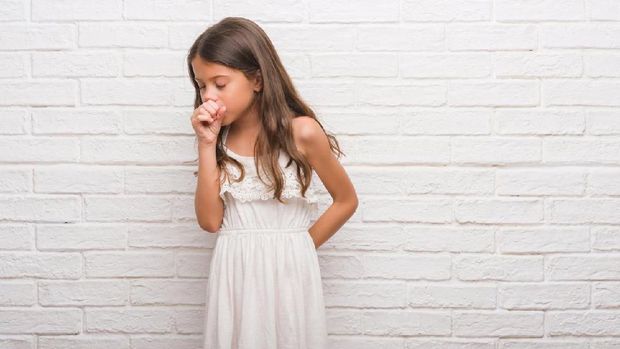 Cute little blond girl coughing in her elbow isolated on white- the technique  recommended by the U.S. Centers for Disease Control and Prevention and the American Academy of Pediatrics.