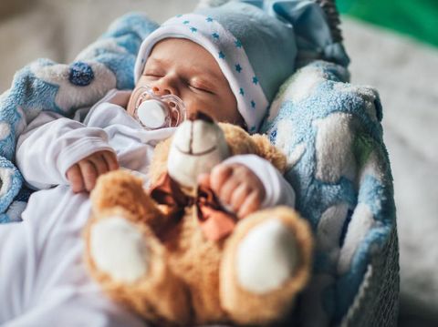 Newborn baby boy sleeping in crib with teddy bear
