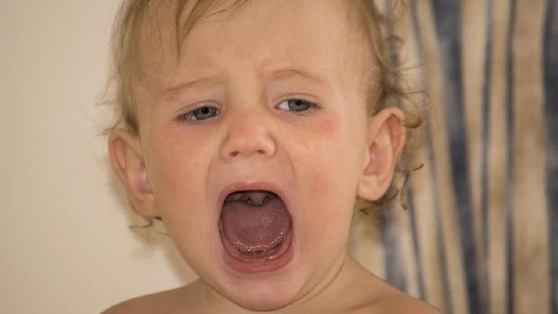 One year old baby crying in bed with a teddy bear