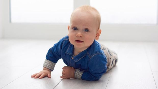 Portrait of a cute little baby in blue denim shirt laying on the floor. Candid image of young baby playing at home