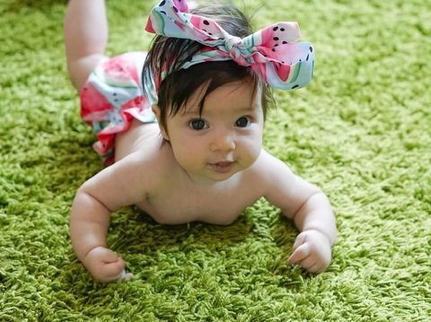 Cute baby girl with hair bow lying on the rug.