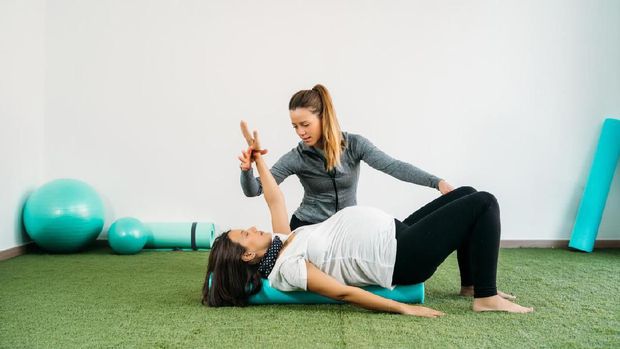 Pregnant woman doing fitness ball and pilates exercise with coach. Happy future mother preparing for childbirth.
