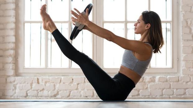 Young sporty attractive woman doing toning pilates exercise for abs, balance Paripurna Navasana pose with pilates magic circle in hands, working out wearing sportswear, indoor full length, yoga studio