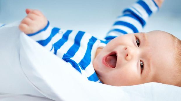 happy little boy lying in the bed. Cute four month old baby in striped sleepsuit at home.