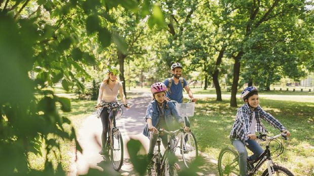 Family riding bicycle in the public park together. Cycling and enjoying the sunny day