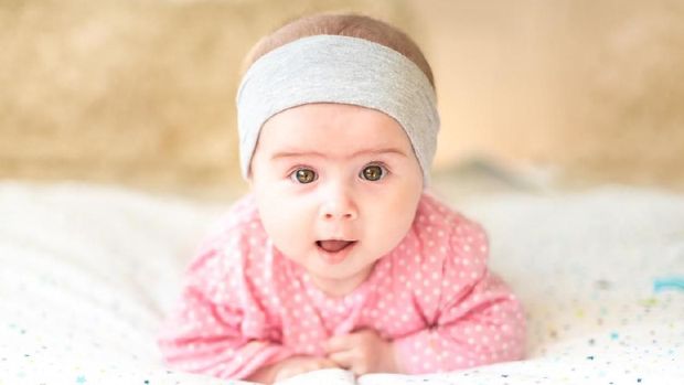 Adorable baby girl with grey headband looking towards camera and smiling. Health concept. 6 months old baby