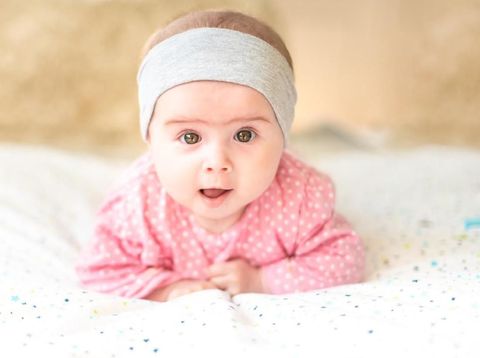 Adorable baby girl with grey headband looking towards camera and smiling. Health concept. 6 months old baby