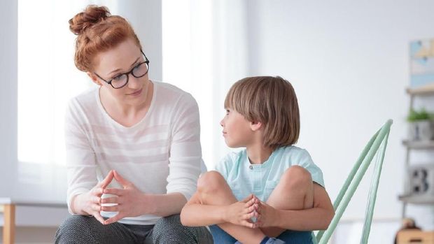 Young female school psychologist having serious conversation with smart little boy at office