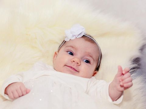 little baby on a light fur in white dress with a bow in the hair