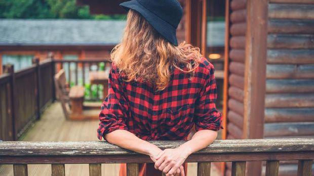 ilustrasi Kemeja Flannel A young woman wearing a hat is relaxing on the porch of a log cabin