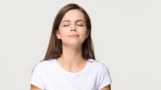 Happy calm teen girl enjoying good smell or pleasant fragrance, serene mindful young woman taking deep breath feel no stress free inhaling fresh air relaxing isolated on white grey studio background