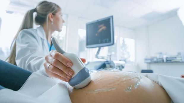 Close-up of pregnant woman relaxing and sitting on the side on the sofa. Holding a hands on the tummy.