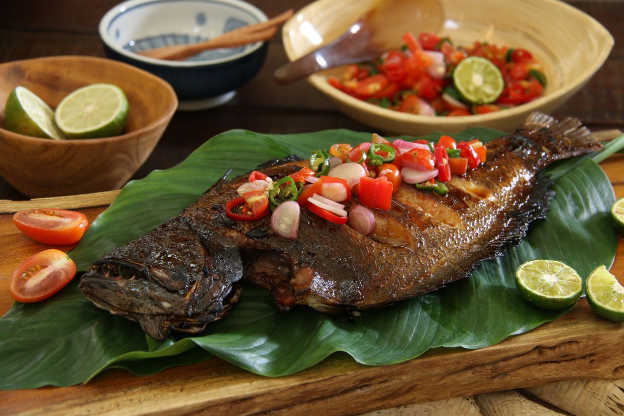 Ikan Bakar Dabu-Dabu, the popular grilled fish dish from Manado, North Sulawesi. The fish is lightly seasoned then grilled; served with the spicy tomato salsa. The fish is plated on a wooden serving block lined with layers of broad green leaves. Accompanied with extra salsa and limes.