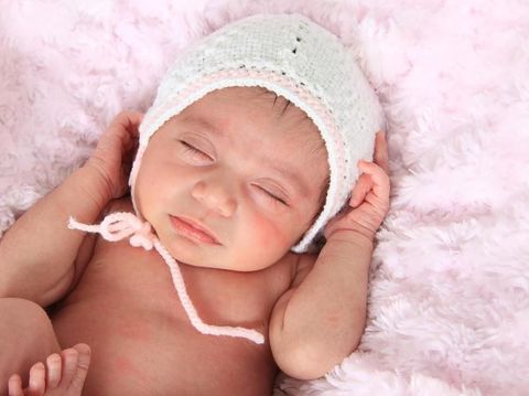 Newborn baby girl of Caucasian and Asian heritage, wearing a knitted bonnet.
