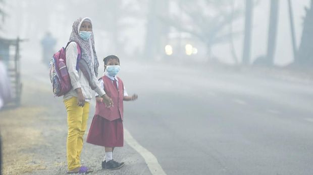 Seorang siswa bersama orang tuanya mengenakan masker  saat menunggu angkutan umum, di Palembang, Sumatera Selatan, Senin (23/9/2019). Pemerintah Kota Palembang meliburkan siswa sekolah selama tiga hari, 23-25 September 2019 akibat asap yang dapat membahayakan kesehatan. ANTARA FOTO/Mushaful Imam/wpa/ama.