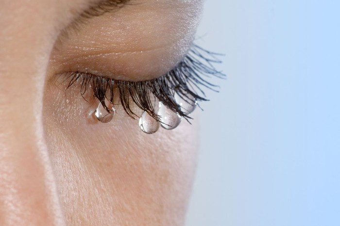 Womans eye with several teardrops hanging on her eyelashes