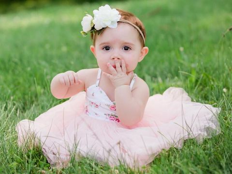 Cute one year old caucasian girl outside in grass wearing a pink summer dress and floral headband