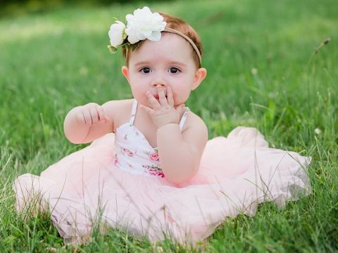 Cute one year old caucasian girl outside in grass wearing a pink summer dress and floral headband