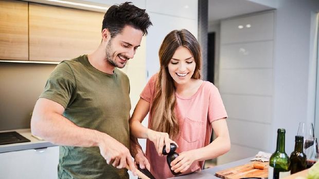 Cute joyful couple cooking together and adding spice to meal, laughing and spending time together in the kitchen