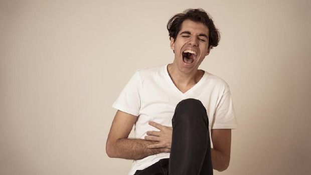 Portrait of young millennial funny male having fun bursting into laughing loudly after hearing humor anecdotes and jokes. Isolated against neutral background. In positive human emotions expressions.