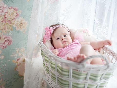 adorable smiling newborn baby girl lies at basket with flowers