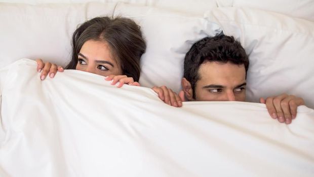 Portrait of a scared couple in bed with man and woman looking very anxious