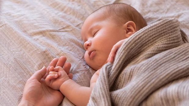 Close-up of sleeping baby hand in the mother's hand on the bed. New family and baby sleep concept