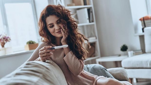 Attractive young women looking at pregnancy test and smiling while sitting on the sofa at home