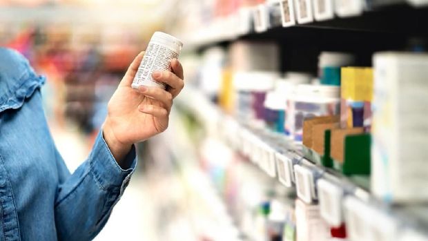 Customer in pharmacy holding medicine bottle. Woman reading the label text about medical information or side effects in drug store. Patient shopping pills for migraine or flu. Vitamin or zinc tablets.