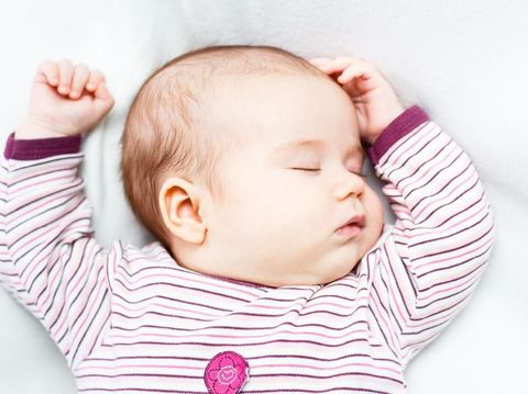 Portrait of a beautiful baby girl sleeping on white blanket in bed. Female newborn face closeup.