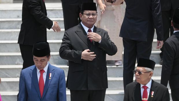 Newly inaugurated Defense Minister Prabowo Subianto, center, adjusts his tie as Indonesian President Joko Widodo, left, and his deputy Ma'ruf Amin, right, take their position for a group photo with other new cabinet ministers after the swearing-in ceremony of the new cabinet at Merdeka Palace in Jakarta, Indonesia, Wednesday, Oct. 23, 2019. Widodo named Subianto, his defeated election rival, a former general linked to human rights abuses, as his defense minister Wednesday and added entrepreneurs and technocrats to his Cabinet to address slowing growth in Southeast Asia's largest economy. (AP Photo/Dita Alangkara)