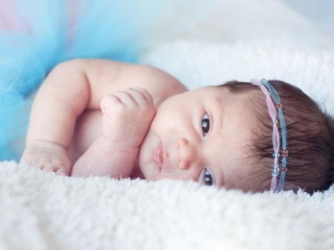 Newborn baby girl. Portrait of a newborn girl with a fluffy skirt  and  the pink - blue  Headbands  with beads. Baby is looking straight.