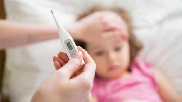 Close-up thermometer. Mother measuring temperature of her ill kid. Sick child with high fever laying in bed and mother holding thermometer. Hand on forehead.