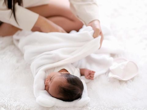 Newborn baby was swaddling with white cloth by her mother and the activity is on bed.