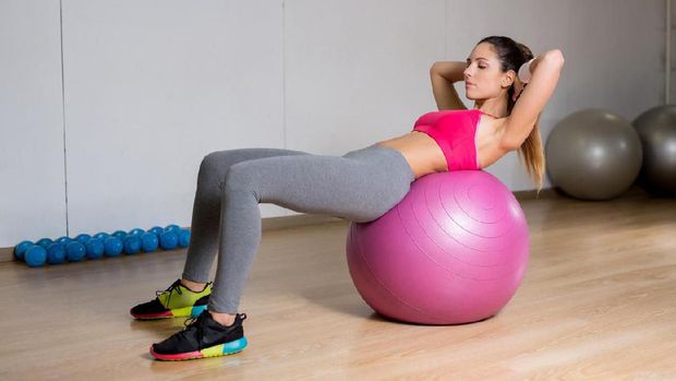 Young sporty woman leaning on fitball while doing press-ups in gym