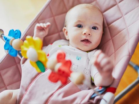 Adorable baby girl sitting in bouncer and playing with colorful toys