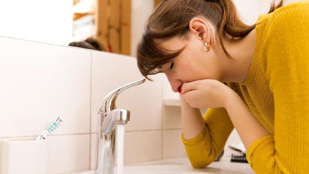 Young vomiting woman near sink in bathroom