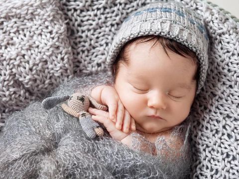 Sweet newborn baby sleeps in a basket. Beautiful newborn boy with bear toy.