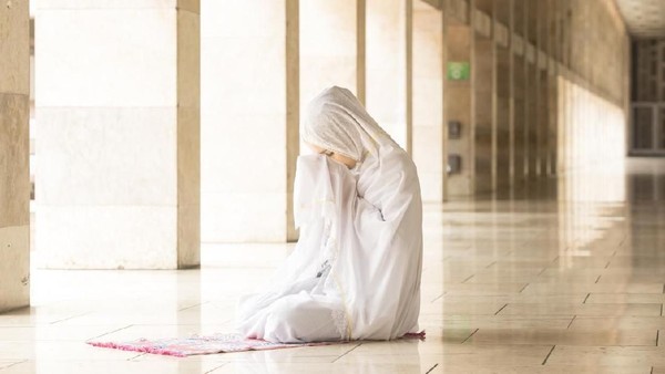 Young muslim woman praying in mosque while wearing prayer veil