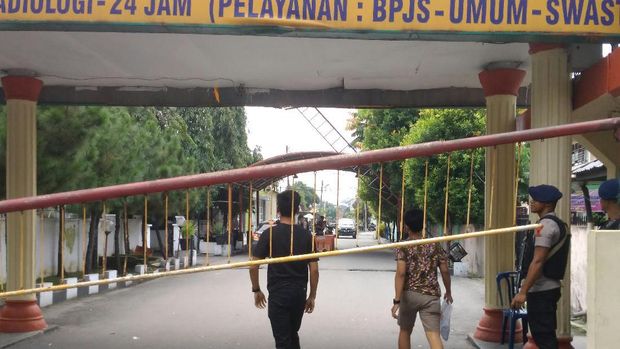 Petugas bersenjata lengkap bersiaga di depan gerbang masuk rumah sakit. 