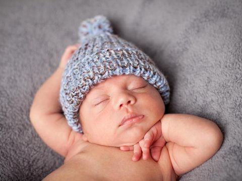Close up, color image of a mixed race newborn baby boy sleeping peacefully and wearing knit cap, on gray textured background.