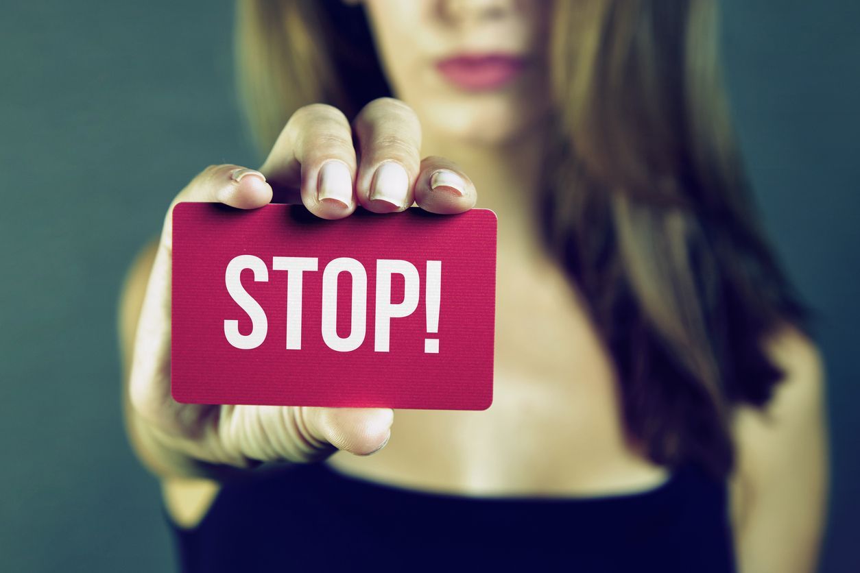 Young woman holding stop card on dark background