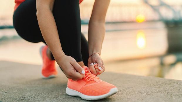 Close up of sporty woman tying shoelace while kneeling outdoor, In background bridge. Fitness outdoors concept.