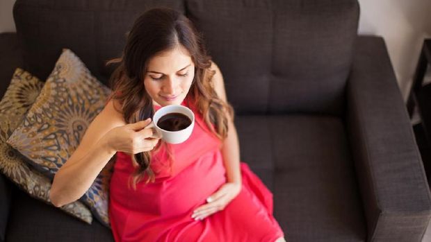 High angle view of a young pregnant woman drinking a cup of coffee at home