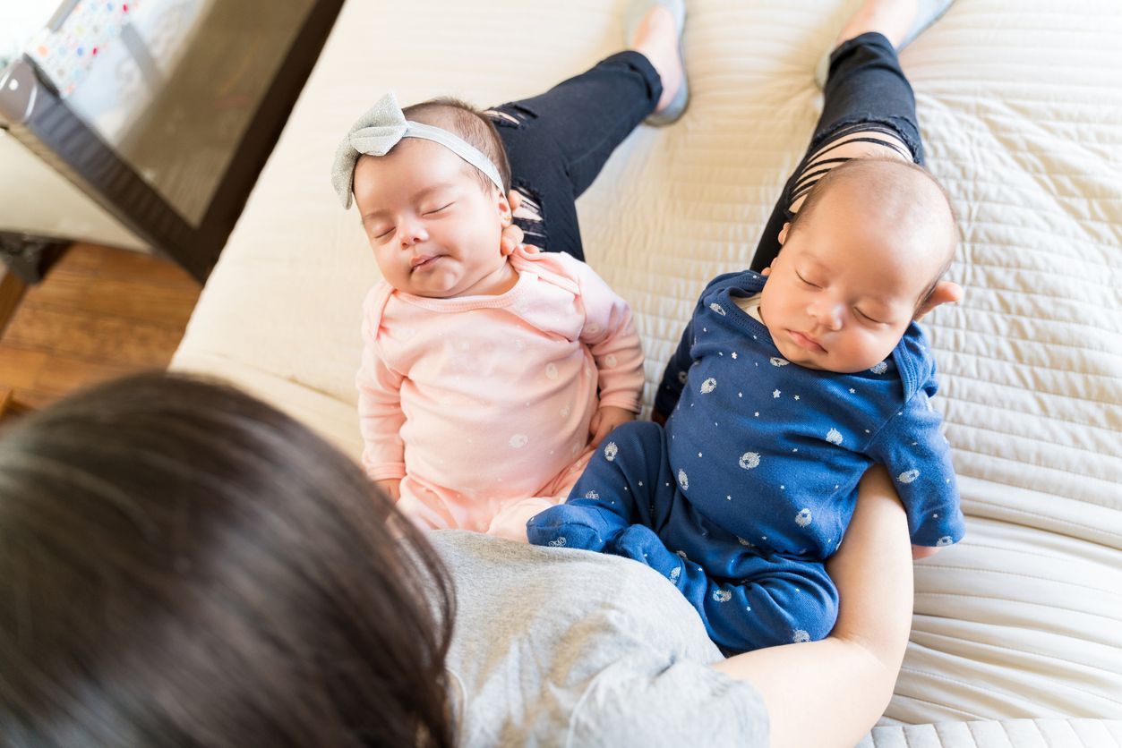 High angle view of mother holding adorable twin kids on bed