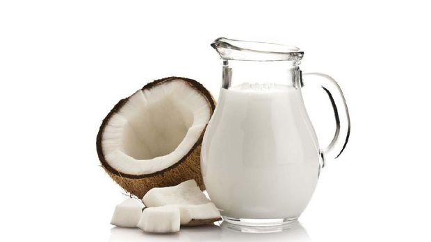 Coconut milk in a little jar and half coconut with pieces isolated on reflective white background.