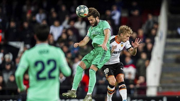 Pemain Real Madrid, Nacho (tengah), berduel dengan pemain Valencia Daniel Wass di Stadion Mestalla, Senin (16/12) dini hari WIB. Laga berakhir imbang 1-1. (Foto: Alberto Saiz/AP Photo)